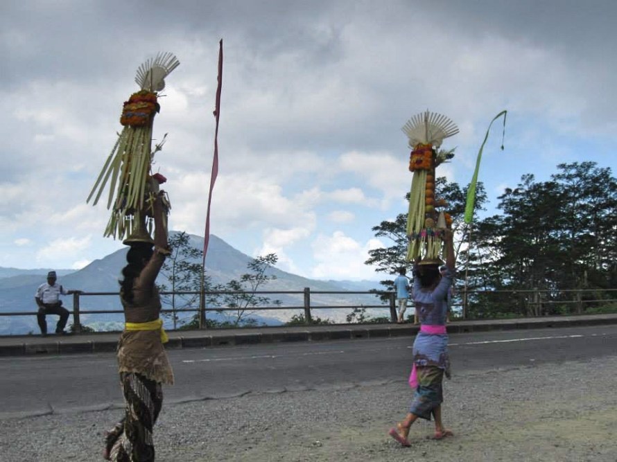 Wanita lokal Bali membawa Gebogan (persembahan/sesajen) di atas kepala (tradisi Nyunggi) saat perjalanan di Kintamani, menunjukkan keanggunan budaya lokal.
