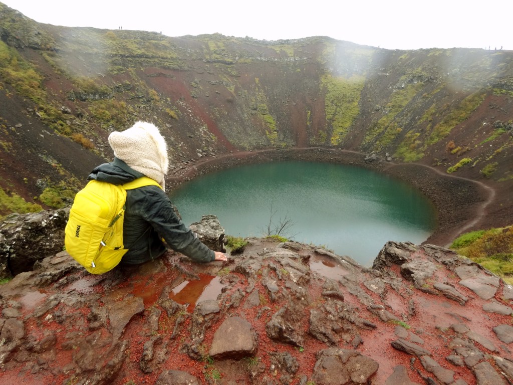 duduk di tepi Danau Kerið di Iceland dengan pemandangan kawah vulkanik dan air biru kehijauan